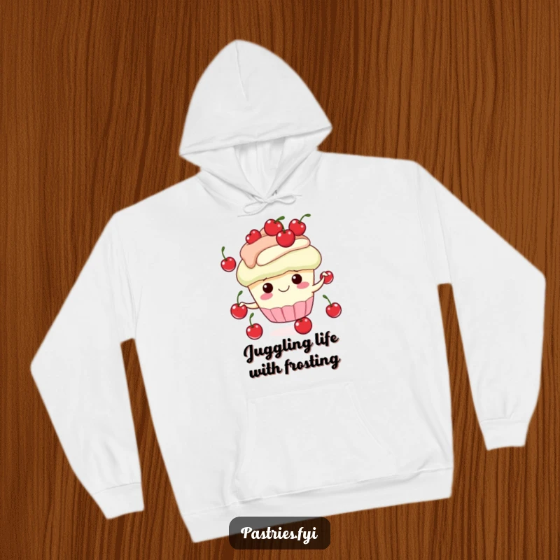 Funny hoodie graphic of a smiling cupcake character skillfully juggling small red cherries, offering warmth and a cheerful vibe.