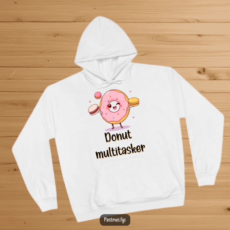 Funny hoodie showing a winking donut character juggling three colorful macarons, perfect for a cozy and cheerful vibe.